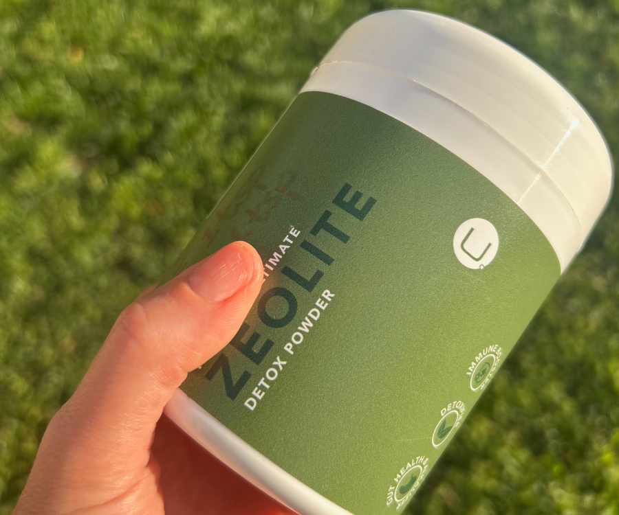 Dr-Ria-Smit-nordens-ultimate-zeolite-detox-powder-product Hand holding Nordens Ultimate Zeolite Detox Powder container outdoors, showing green label with U logo, gut health, detox, and immune support benefits